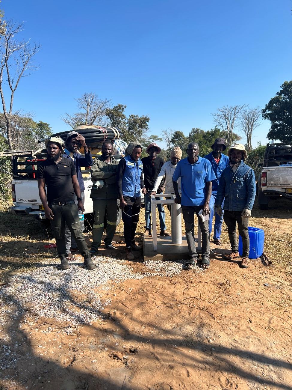 Field team standing at community water point during maintenance works